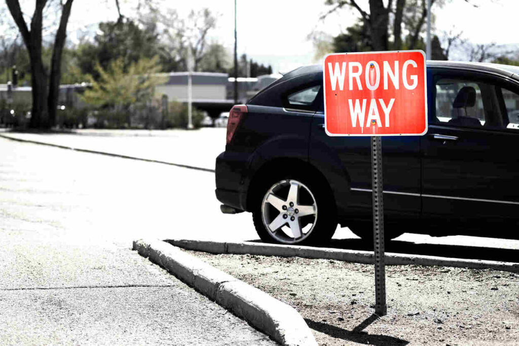 Red WRONG WAY road sign next to a car, illustrating the cause of dangerous North Carolina wrong-way crashes and potential injuries.