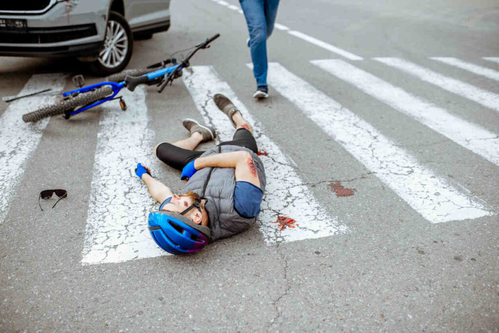 Cyclist injured in a road accident lying on a crosswalk with a bike nearby, highlighting the risks of cycling accidents and the importance of driver caution.