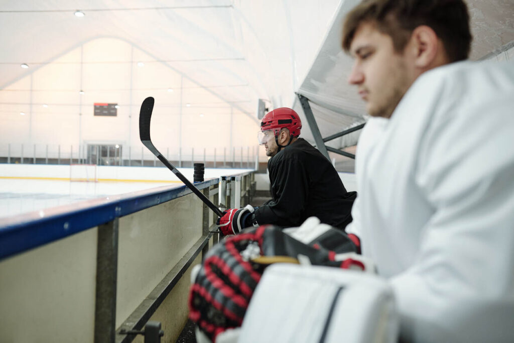 Two hockey players on the bench, one with a stick, symbolizing sports injury and workers' comp.