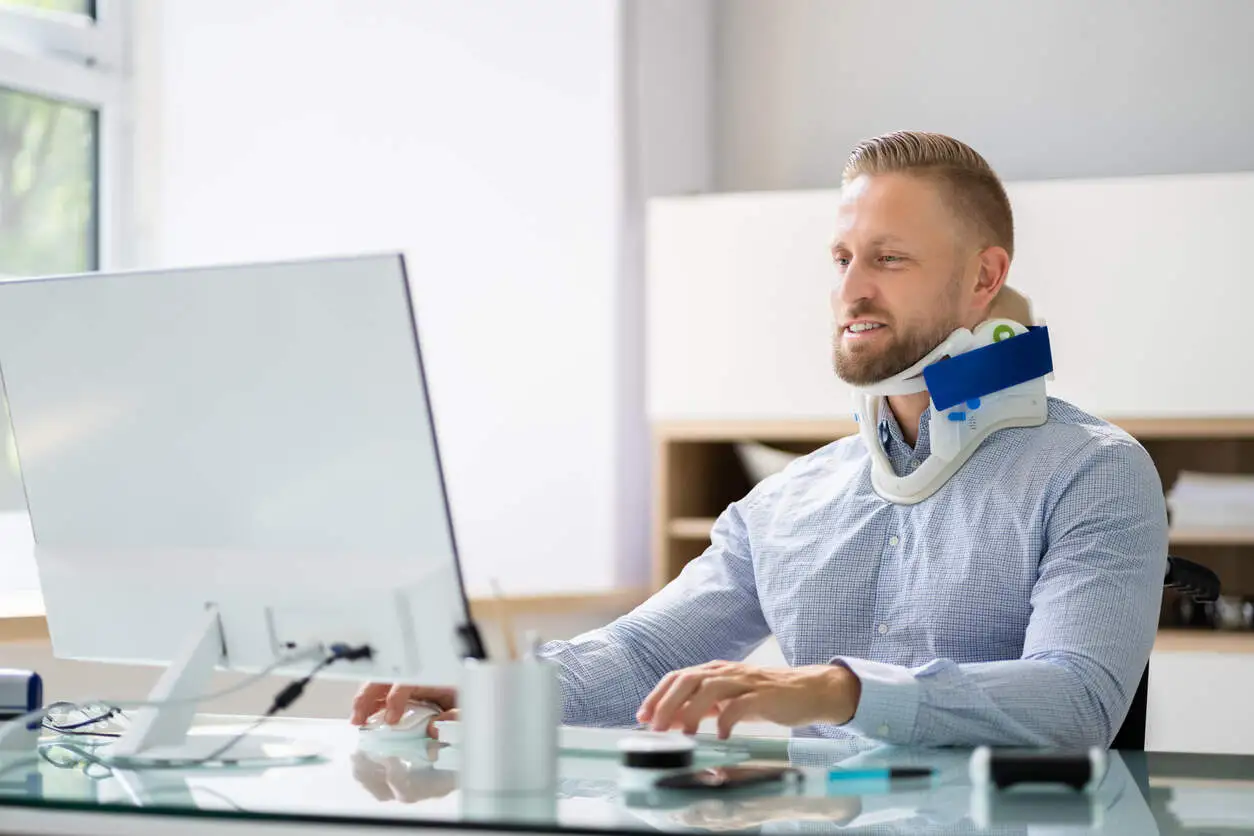 Business owner with neck injury working on computer, highlighting the challenges for executives in North Carolina